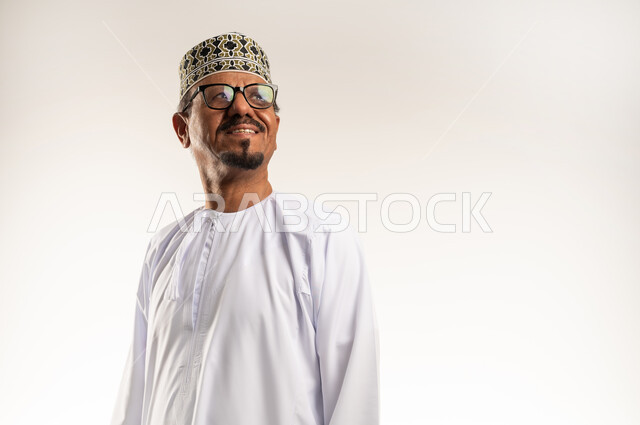 رؤية الأشياء البعيدة، الاهتمام بالمظهر الخارجي, ارتداء أزياء عمانية تقليدية، بورتريه مقرب لرجل عربي خليجي عماني يرتدي الدشداشه و الكمه يلبس النظارات الطبية وينظر إلى مكان ما بعيد بإيماءات التركيز والشرود, خلفية بيضاء