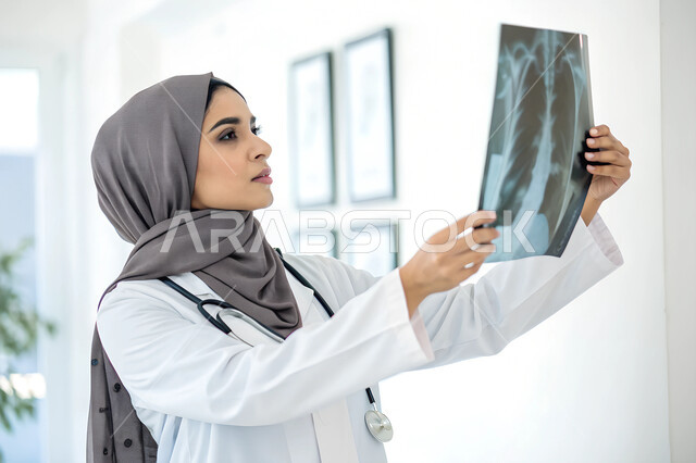 التطور والتقدم في المجال الطبي، استخدام التقنية والتكنولوجيا في البحث الصحي, طبيبة عربية خليجية سعودية محجبة ترتدي المعطف والسماعة الطبية تحمل صورة الأشعة للمريض تنظر إليها لمعاينتها, مفهوم التصوير الشعاعي, الكشف عن المرض والحالة غير الواضحة