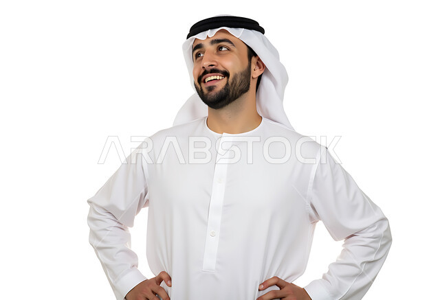 مفهوم الأناقة والاهتمام بالمظهر الخارجي، بورتريه مقرب لرجل عربي خليجي إماراتي يرتدي الكندوره والغترة يقف ويضع يديه على خصره وينظر إلى مكان ما بإيماءات السعادة والسرور، الضحك والرضا والشعور بالفرح، خلفية بيضاء
