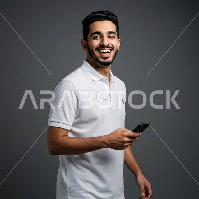Browsing social networking sites, chatting with friends and relatives via mobile, using a modern and advanced technical device, close-up portrait of a smiling Saudi Arabian Gulf man wearing casual clothes holding a mobile phone in his hand, gray background
