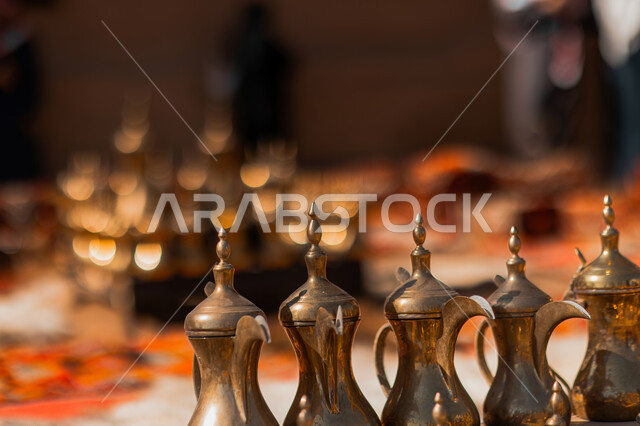 Preparing Arabic coffee in the traditional way in Al-Ula Governorate in Saudi Arabia, a close-up of copper coffee pots, ancient archaeological sites and markets that attract tourists and visitors, generous hospitality and good reception in the Kingdom, antiquity and authenticity in Gulf customs and traditions