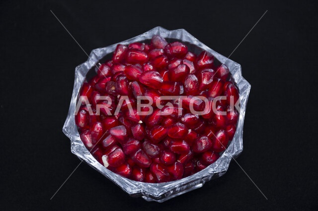 Close-up of a bowl full of delicious fresh pomegranate seeds, fresh pomegranate fruit, a bowl full of delicious pomegranate seeds depicted on a black background, pomegranate seeds
