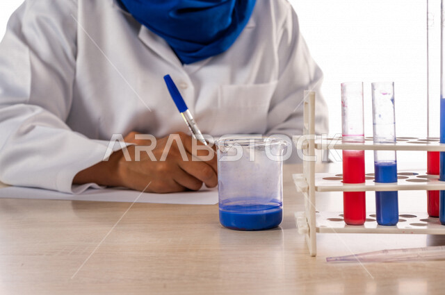 طبيبة مختبرات طبيه عربيه سعوديه خليجيه ترتدي معطف أبيض، إجراء التفاعلات الكيميائيه  داخل المختبر، تجارب و أبحاث طبيه، تسجيل النتائج و الملاحظات, دراسات وتحاليل, مواد كيميائيه
