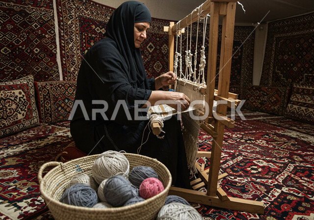 الفن التراثي الحرفي التقليدي، نقش وزخرفة من التراث السعودي، معمل ومصنع لحياكة وغزل السجاد، مهنة وحرفة شعبية، سيدة عربية خليجية سعودية محجبة ترتدي العباءة تقوم بنسج السجادة، منتج صناعي محلي وطني