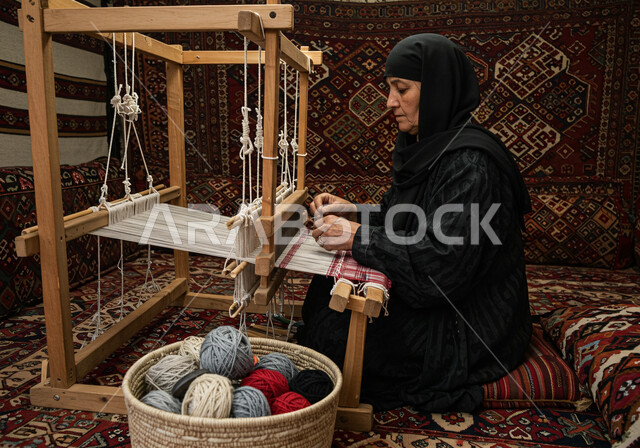 مهنة وحرفة شعبية، معمل ومصنع لحياكة وغزل السجاد، سيدة عربية خليجية سعودية محجبة ترتدي العباءة تقوم بنسج السجادة، نقش وزخرفة من التراث السعودي، الفن التراثي الحرفي التقليدي، منتج صناعي محلي وطني