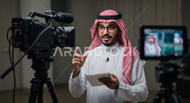 كواليس تقديم البرامج والنشرات الإخبارية، صورة مقربة لإعلامي عربي خليجي سعودي يرتدي الثوب التقليدي والشماغ يقوم بتقديم نشرة تلفيزيونية أمام الكاميرا، قراءة الموجز الإخباري، أخبار العالم والمملكة العربية السعودية، كتابة وتدوين الملاحظات