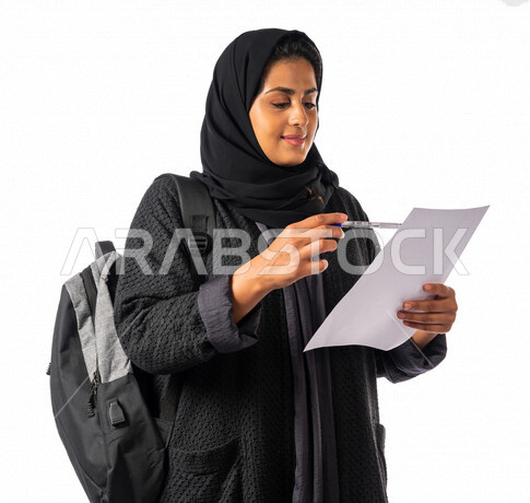 A Saudi Arabian Gulf university student holding a paper and pen in her hand, reviewing a worksheet, a diligent student, her lessons tickets, schools and universities, education in the Kingdom of Saudi Arabia