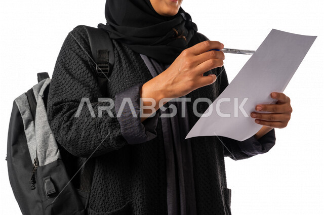 A Saudi Arabian Gulf university student holding a paper and pen in her hand, reviewing a worksheet, a diligent student, her lessons tickets, schools and universities, education in the Kingdom of Saudi Arabia