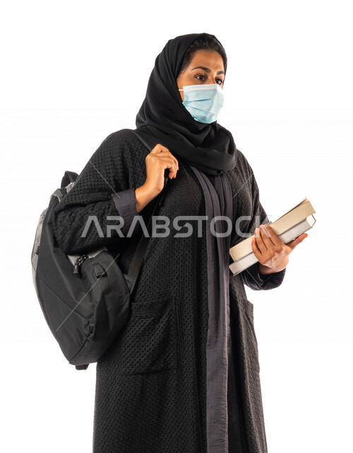 A Saudi Arabian Gulf university student carrying books and a university bag, preparing for the new academic year, obligating wearing a muzzle to avoid infection with the Corona virus, schools and universities, education in the Kingdom of Saudi Arabia