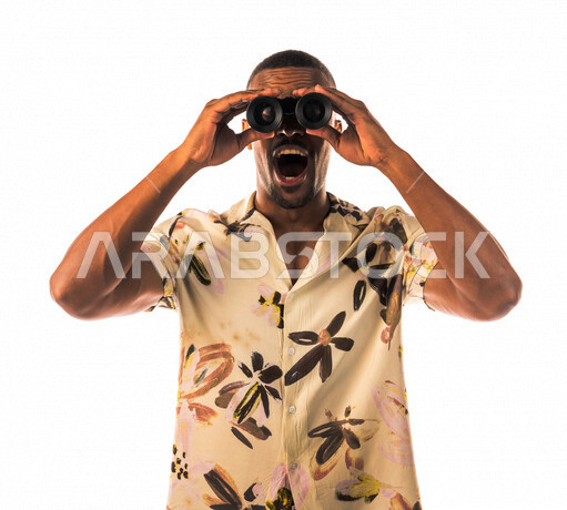 بورتريه لشاب اسمر عربي خليجي سعودي، ينظر من خلال الناظور، إيماءات وجه تدل على الدهشة والتعجب، الاستكشاف و المغامرة، فريق الكشافة، ملابس كاجوال، بشرة سمراء، خلفية بيضاء