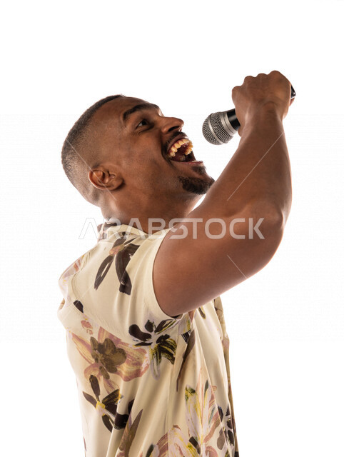 بورتريه لشاب اسمر عربي خليجي سعودي يمسك المايكروفون، تقديم العروضات المسرحية، القاء الخطابات، الحوارات والنقاشات، اداء تمثيلي، الفن المسرحي الغنائي، ملابس كاجوال، بشرة سمراء، خلفية بيضاء