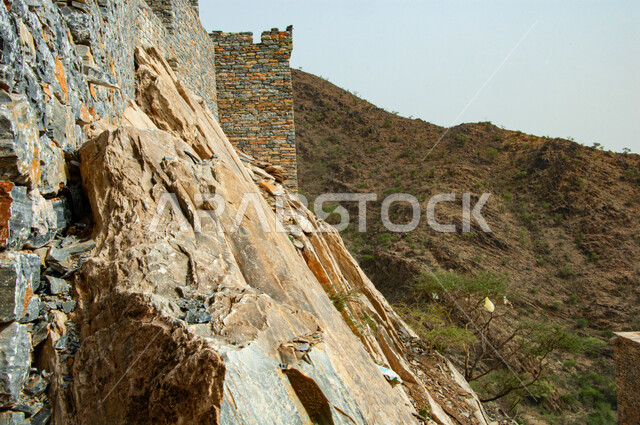 Rocky terrain, peaks and mountain heights during the day, a heritage stone building and house in the ancient village of Dhi Ain in the city of Al Baha in the south of the Kingdom of Saudi Arabia, a famous historical tourist area, a natural place that attracts and attracts tourists from all over the world