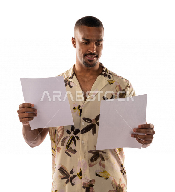 بورتريه لشاب أسمر عربي خليجي سعودي، يقف ويحمل بيده مجموعة من الاوراق، التحقق والتدقيق في الاوارق، ارتداء ملابس كاجوال، بشرة سمراء، خلفية بيضاء