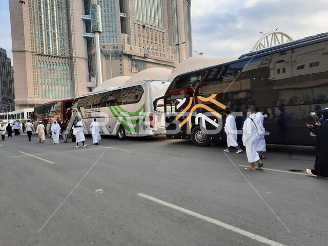 أداء مناسك الحج والعمرة, باصات نقل الحجاج والمعتمرين إلى مكة المكرمة, أماكن ومعالم دينية إسلامية مقدسة في المملكة العربية السعودية, وصول مجموعة من زوار بيت الله الحرام الى موقف الحافلات خارج المسجد الحرام، الفن الهندسي المعماري للفنادق وبرج الساعة