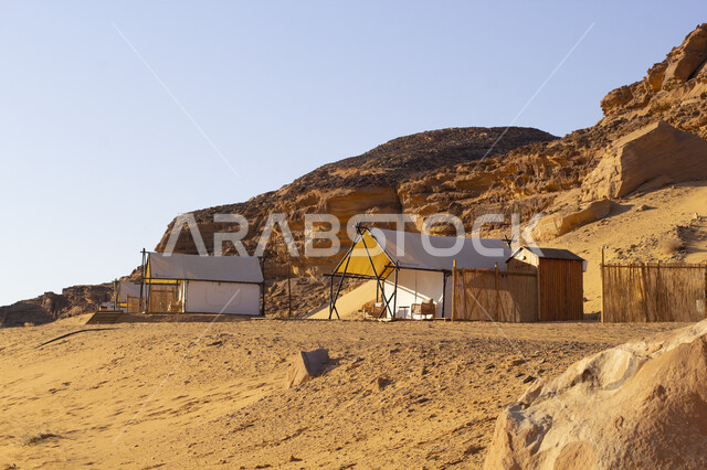 Adventure and recreational trip, camping in the desert areas of Al-Ula Governorate, a famous tourist place and area in the desert of the Kingdom of Saudi Arabia, a group of white tents on the soft golden sand, rock formations and formations in the desert, a youth session and outing in the wilderness