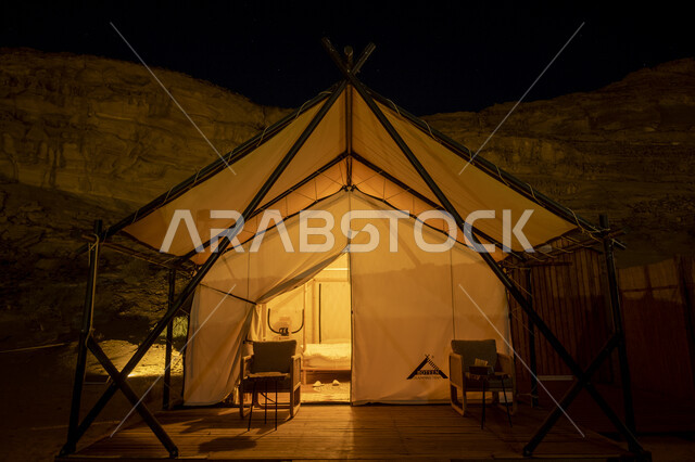 جلسة وكشتة شبابية في البرية، التكوينات والتشكيلات الصخرية في الصحاري، خيمة بيضاء في صحراء المملكة العربية السعودية في الليل، مغامرة ورحلة ترفيهية، التخييم في المناطق الصحراوية في محافظة العلا، مكان ومنطقة سياحية مشهورة