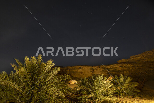 Rock formations and formations in mountainous areas, famous tourist places in the Kingdom of Saudi Arabia, a lighted recreational park and farm in the village of Al-Ula in Al-Ula Governorate at night, interest in planting natural green plants and trees in the desert
