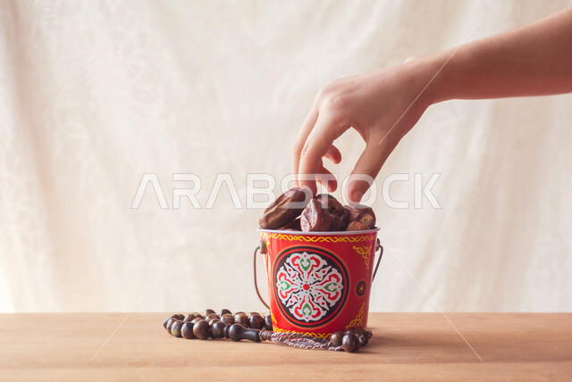 وجبة ذات قيمة غذائية عالية, ضيافة عربية تقليدية, الرطب العربي الخليجي الفاخر, جودة المحصول الزراعي في المملكة العربية السعودية, صورة مقربة ليد تأخذ حبة من التمر السكري الصحي وبجانبها مسبحة, منتج محلي وطني سعودي