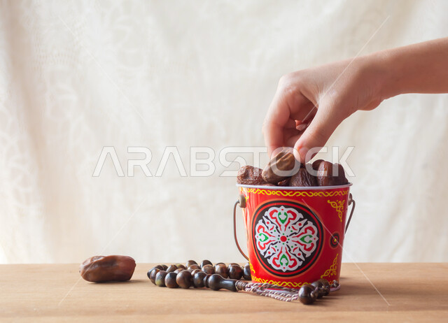 ضيافة عربية تقليدية, وجبة ذات قيمة غذائية عالية, الرطب العربي الخليجي الفاخر, جودة المحصول الزراعي في المملكة العربية السعودية, صورة مقربة ليد تأخذ حبة من التمر السكري الصحي وبجانبها مسبحة, منتج محلي وطني سعودي