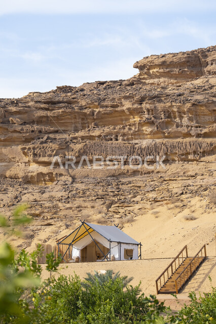 التخييم في المناطق الصحراوية في محافظة العلا، كشتة وجلسة شبابية في البرية، مكان ومنطقة سياحية مشهورة في صحراء المملكة العربية السعودية، مغامرة ورحلة ترفيهية، خيمة بيضاء على الرمال الذهبية الناعمة، التكوينات والتشكيلات الصخرية في الصحاري