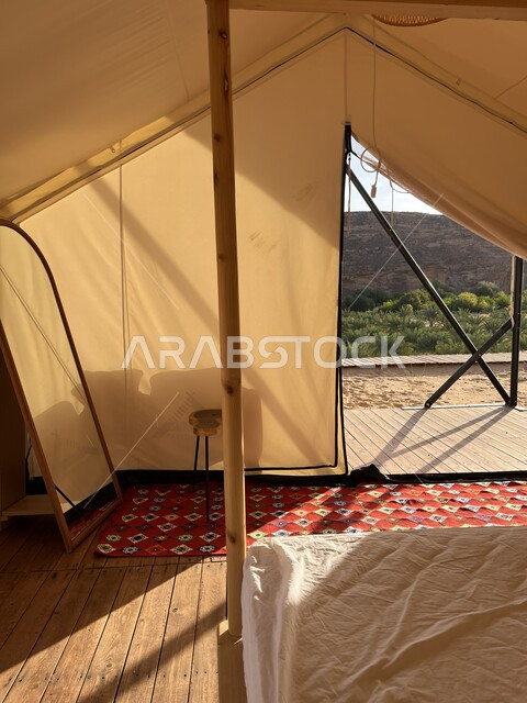 جلسة وكشتة شبابية في البرية، مكان ومنطقة سياحية مشهورة، التخييم في المناطق الصحراوية في محافظة العلا، التكوينات والتشكيلات الصخرية في الصحاري، صورة من داخل خيمة بيضاء على الرمال الذهبية الناعمة، مغامرة ورحلة ترفيهية