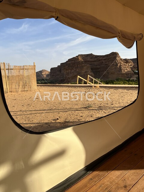 التخييم في المناطق الصحراوية في محافظة العلا، التكوينات والتشكيلات الصخرية في الصحاري، مكان ومنطقة سياحية مشهورة، جلسة وكشتة شبابية في البرية، صورة من داخل خيمة بيضاء على الرمال الذهبية الناعمة، مغامرة ورحلة ترفيهية