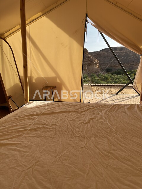 التكوينات والتشكيلات الصخرية في الصحاري، التخييم في المناطق الصحراوية في محافظة العلا، مكان ومنطقة سياحية مشهورة، جلسة وكشتة شبابية في البرية، صورة من داخل خيمة بيضاء على الرمال الذهبية الناعمة، مغامرة ورحلة ترفيهية