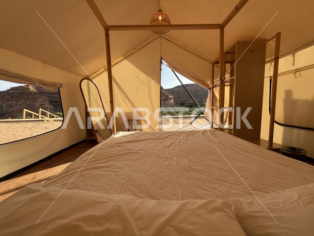 Rock formations in the desert, camping in the desert areas of AlUla Governorate, a famous tourist place and area, a youth session and outing in the wilderness, a picture from inside a white tent on the soft golden sand, an adventure and a recreational trip
