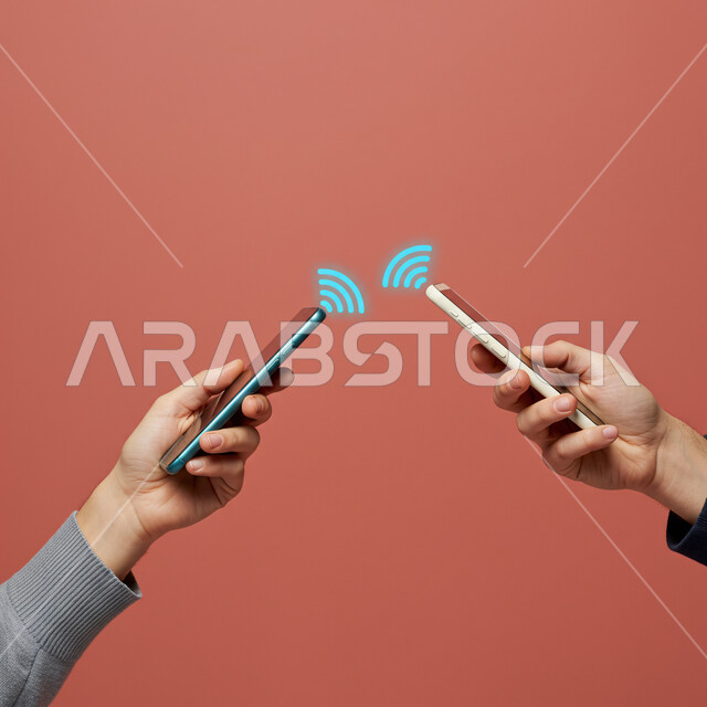 ربط الجوالات عبر شبكات اتصالات الواي فاي، استخدام الأجهزة التكنولوجية الحديثة، تطور الشبكة الرقمية، الذكاء الاصطناعي وتكنولوجيا المستقبل المتقدم، بورتريه مقرب ليدي رجلين عربيين خليجيين سعوديين يمسكان الهواتف المحمولة بأيديهم، أيقونات هولوجرامية مضيئة، خلفية حمراء