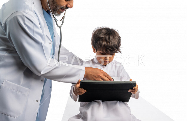 بورتريه لطبيب خليجي سعودي مع طفل صغير ، إستخدام جهاز التابلت ، مفهوم الطب والرعاية الصحية ، الفحص الطبي للأطفال ، تقديم الرعاية والخدمات الصحية ، مهن ووظائف طبية ، يفحص الطبيب قلب الطفل عبر سماعة الأذن ، موعد مع الطبيب لتلقي العلاج