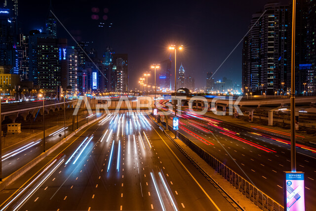 حركة مرور السيارات في الشارع, المباني والمنشآت المضيئة في الليل بمدينة دبي, الفن الهندسي المعماري لبناء الأبراج وناطحات السحاب على الطراز الحديث, مفهوم التقدم والتطور العمراني, مكان سياحي مشهور في الإمارات العربية المتحدة