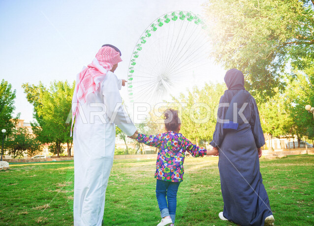 An angle photo from the back of a Saudi Arabian Gulf family spending their time with fun and entertainment in the game city in the daytime setting, spending enjoyable family times in the amusement park, entertainment and entertainment, summer vacation ent