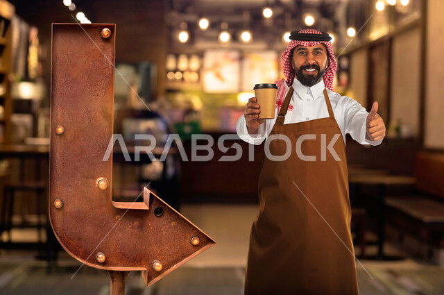 صورة لرجل عربي سعودي خليجي داخل مقهى، يرفع اصبع الابهام لاعلى للاعجاب والرضى ، يحمل بيده كوب القهوة الساخن ، اعداد وتجهيز القهوة ، تقييم خدمات المقهى ، القهوة العربية السعودية، خدمة التوصيل السريع للمشروبات الساخنة