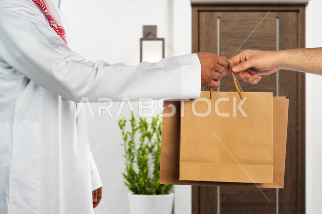 A Saudi Arabian Gulf man working in the delivery of orders and goods delivers goods to customers, a customer receives his purchases, online shopping, online orders, smart shopping, reliable shipping and delivery process, delivery representative, express d
