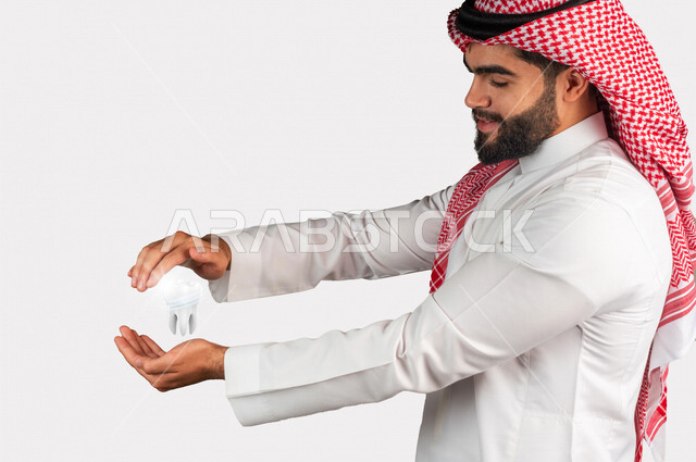 صورة مقرّبة لرجل عربي سعودي خليجي يحمل بين يديه مجسم هولوجرامي لضرس ، طب و صحة الأسنان ، حماية الأسنان وعلاج التسوس.