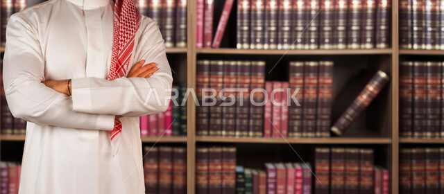 صورة مقربة لرجل عربي سعودي خليجي مكتف اليدين داخل مكتبه , مجموعة من الكتب منظمة داخل رفوف , قراءة وتعلم , كتابة وتأليف .