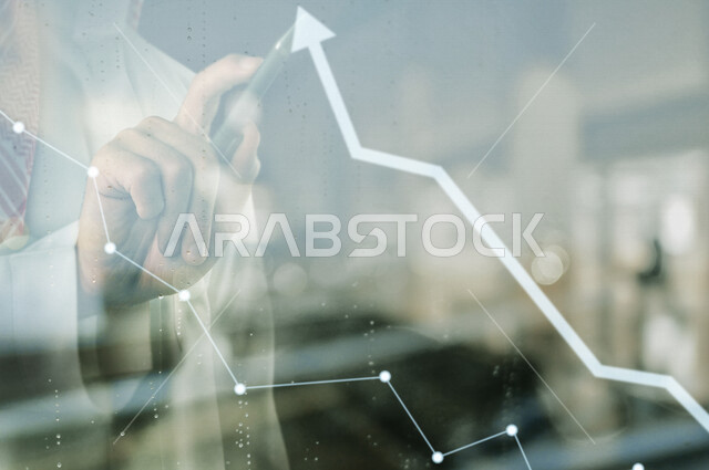 صورة مقربة لرجل عربي سعودي خليجي بيديه قلم تقني ذكي يضغط علي سهم على شاشة برسومات بيانية ثلاثية الأبعاد بتقنية الهولوجرام ، صعود و نزول البورصة المالية ، الاستثمار المالي و الاقتصادي ، التطور الإقتصادي
