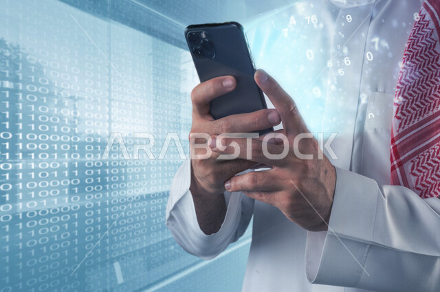 صورة مقربة لرجل عربي خليجي سعودي يقف بجانب شاشة تحتوي لغة الخاصة بالبرمجة و يمسك بيده هاتف محمول مع خروج مجموعة من الأرقام المضيئة المتطايرة بتقنية الهولوجرام ، استخدام تقنية الهولوجرام ثلاثية الأبعاد