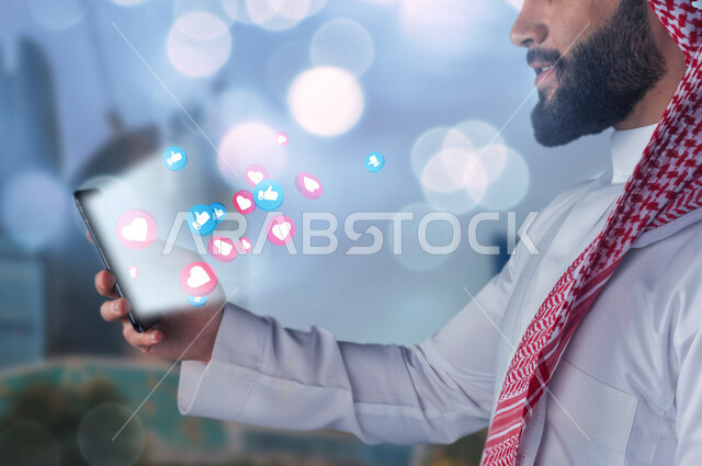 صورة لرجل عربي خليجي سعودي مبتسم يحمل هاتف محمول بيده ، خروج فقاعات متطايرة خاصة بتفاعلات مواقع التواصل الإجتماعي السوشال ميديا ، مجموعة من الاشعارات التفاعلية الخاصة بالسوشيال ميديا ، التفاعل و التواصل الإجتماعي