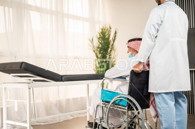 طبيب عربي سعودي خليجي يقوم بتجهيز مريض مسن يجلس على كرسي متحرك لإجراء الفحوصات اللازمة وتلقي العلاج , مفهوم الطب و الرعاية الصحية , مهن ووظائف طبية .