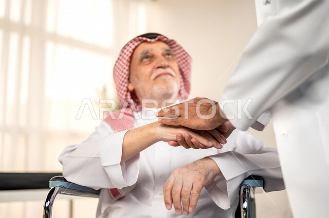 تقديم أفضل الخدمات الصحية لمرضى كبار السن في المستشفى , مريض مسن عربي سعودي خليجي يجلس على كرسي متحرك , يقوم بشكر وتقدير الطبيب لجهوده ورعايته الطبية , مفهوم الطب والرعاية الصحية .