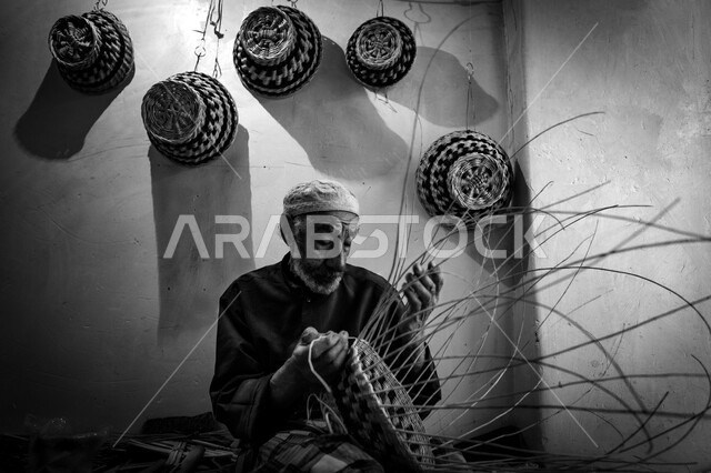 Authenticity and heritage in the Kingdom of Saudi Arabia, an ancient historical handicraft, a traditional folk profession, a local national industrial product, a Saudi Gulf Arab man sitting on the ground weaving palm fronds, using dried palm leaves in making baskets, the Janadriyah Cultural Heritage Festival in Riyadh