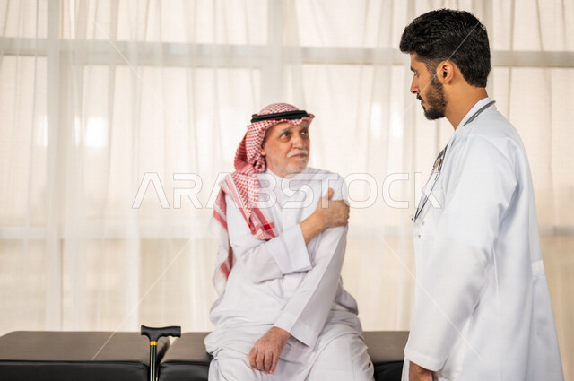 مريض عربي سعودي كبير بالسن يشكو من آلام في الكتف واليد , يقوم الطبيب بفحص المريض والتأكد من سلامة اليد , صحة وأطباء , حالة مرضية , مهن ووظائف طبية , خلفية بيضاء .