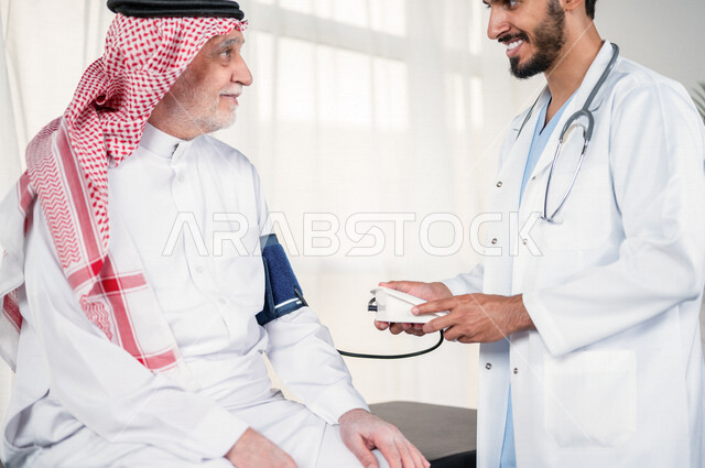 بورتريه لطبيب عربي سعودي خليجي يقوم بقياس ضغط الدم لمريض كبير بالسن ، جهاز لقياس ضغط الدم ، متابعة دورية لفحص ضغط الدم في عيادة خاصة ، حالة مرضية ، خلفية بيضاء .