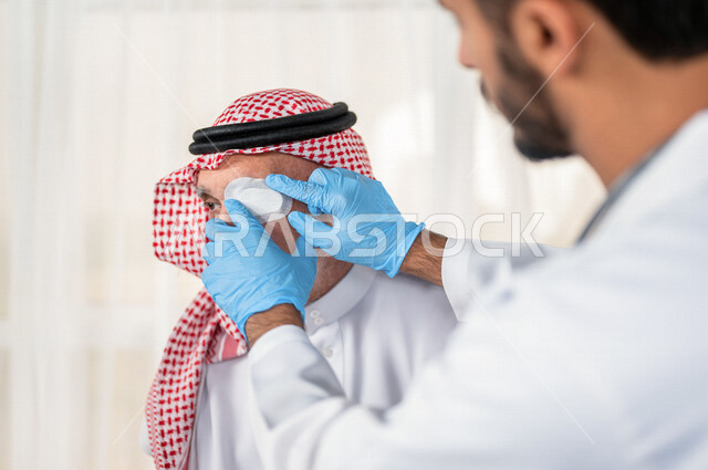 طبيب عيون مختص عربي سعودي خليجي يقوم بتقديم الرعاية الصحية المناسبة لمريض كبير بالسن في المستشفى , يقوم الطبيب بتغطية عين المريض لتحسين نظر العين الأخرى للمريض , مفهوم الطب والرعاية الصحية .