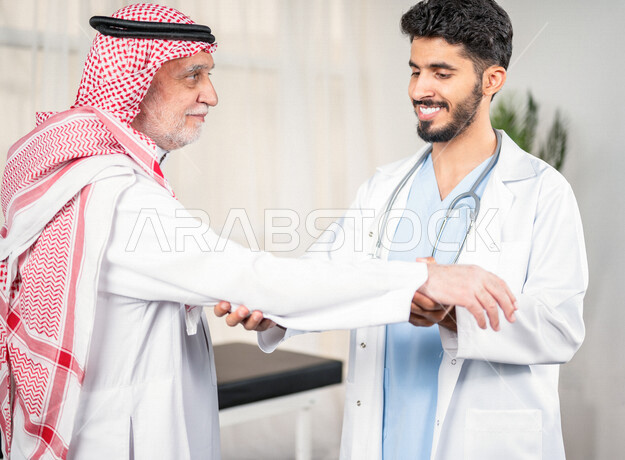مريض عربي سعودي كبير بالسن يشكو من آلام في الكتف واليد , يقوم الطبيب بفحص المريض والتأكد من سلامة اليد , صحة وأطباء , حالة مرضية , مهن ووظائف طبية , خلفية بيضاء .