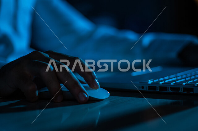 صورة مقربة ليد رجل عربي خليجي سعودي يستخدم الحاسوب المحمول ،يستخدم الفأرة والكتابة من خلال لوحة المفاتيح ، ادخال البيانات، صناعة المحتويات النصية ،التسويق والترويج للمواقع الالكترونية، القيام بالاعمال الادارية ،التعليم الالكتروني
