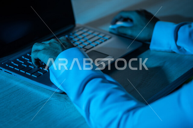صورة مقربة ليد رجل عربي خليجي سعودي يستخدم الحاسوب المحمول ،يستخدم الفأرة والكتابة من خلال لوحة المفاتيح ، ادخال البيانات، صناعة المحتويات النصية ،التسويق والترويج للمواقع الالكترونية، القيام بالاعمال الادارية ،التعليم الالكتروني