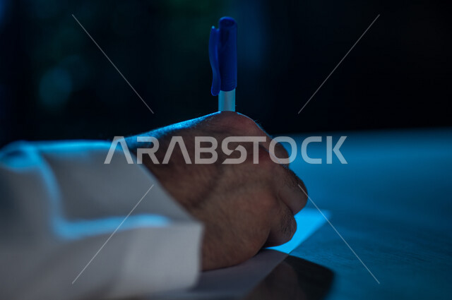 صورة مقربة لرجل عربي خليجي يستخدم الورقة والقلم، يقوم بتدوين الملاحظات الخاصة بالعمل ، اعداد التقارير ومهام العمل ، بحث علمي ، كتابة وتاليف القصص والروايات