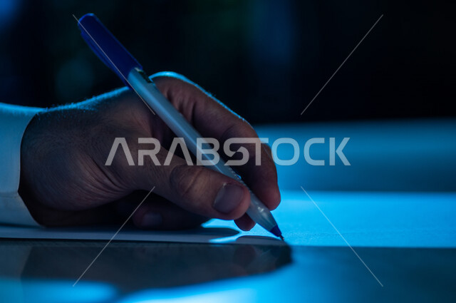 صورة مقربة لرجل عربي خليجي يستخدم الورقة والقلم، يقوم بتدوين الملاحظات الخاصة بالعمل ، اعداد التقارير ومهام العمل ، بحث علمي ، كتابة وتاليف القصص والروايات